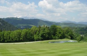 Golfclub Semmering, © Golfclub Semmering Grüne Golfplatzlandschaft mit Teich und bewaldeten Hügeln im Hintergrund.