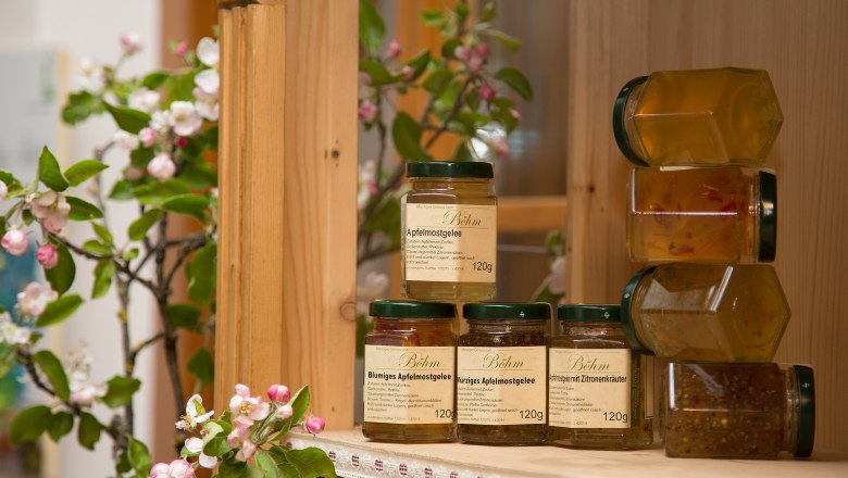 Apple cider jelly from the Böhm gourmet farm, © Genussbauernhof Böhm Jars of apple cider jelly on a wooden shelf, surrounded by blossoming apple branches.
