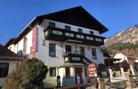 Stelzenheuriger Familie Kamper, © Familie Kamper Ein traditionelles Gasthaus mit Holzverzierungen und einem Schild "Gasthaus Fam. Kamper" vor einem klaren blauen Himmel.