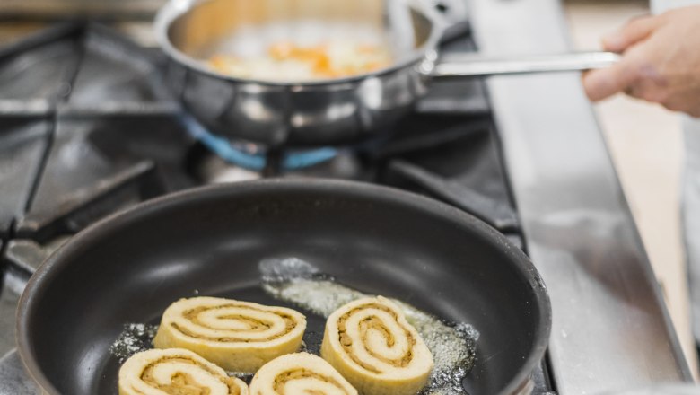 Porcini gomba roulade, © Niederösterreich Werbung/David Schreiber Egy serpenyő három porcini gombás rolóval a tűzhelyen, mellette egy kéz, amely egy másik serpenyőt tart.