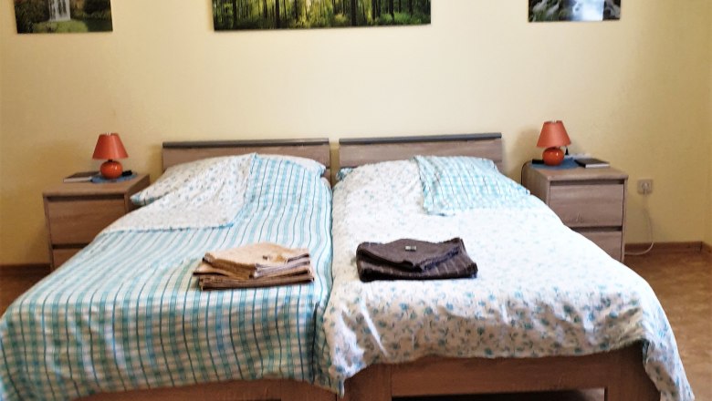 Schlafzimmer, © Stern Schlafzimmer mit zwei Einzelbetten, Nachttischen und Waldlandschaftsbildern an der Wand.