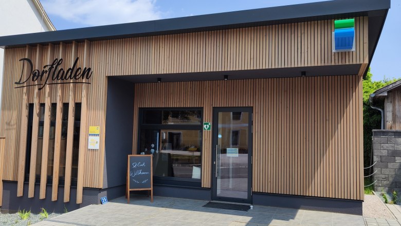 Dorfladen Lichtenegg außen, © Wiener Alpen Außenansicht eines modernen Dorfladens mit Holzverkleidung und einem Willkommensschild vor der Tür.