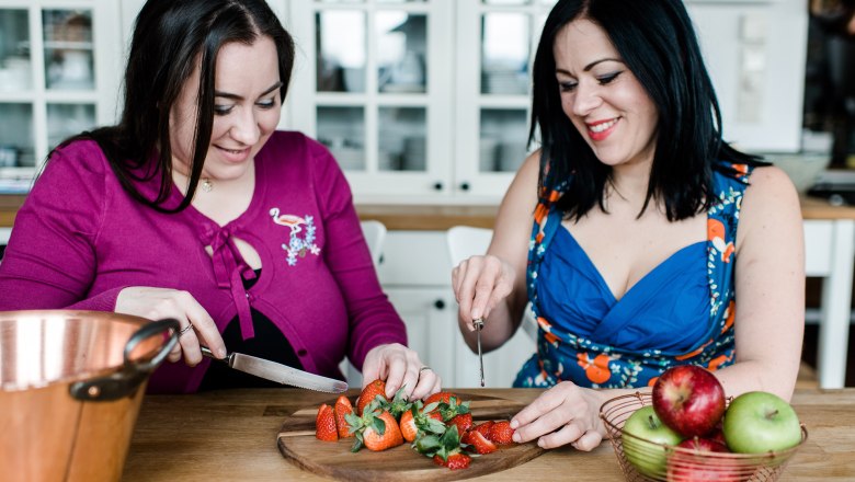 Two women cutting strawberries in a kitchen.