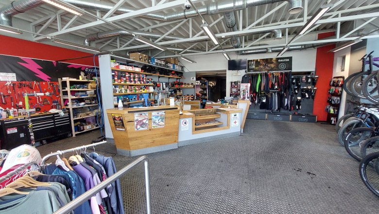 Innenansicht eines Fahrradgeschäfts mit Werkstattbereich, Verkaufstresen und Fahrradzubehör.