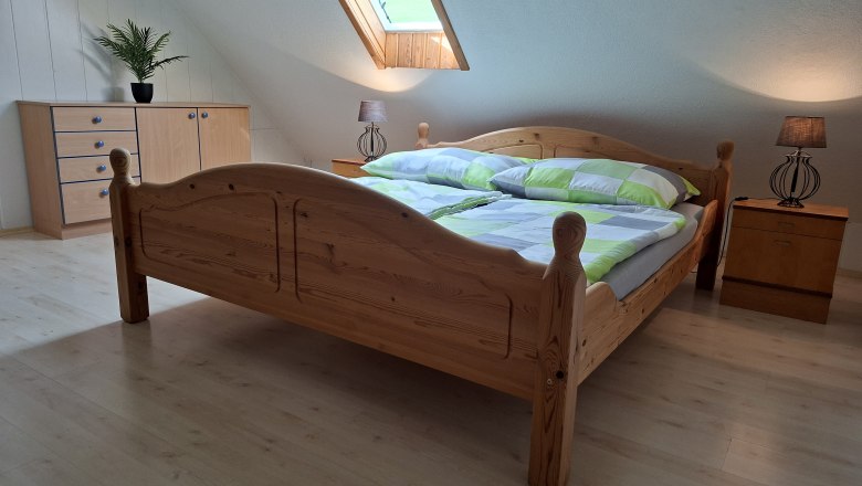 Schlafzimmer mit Holzbett, Kommode, Nachttischlampen und Dachfenster.
