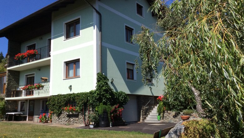 Frühstückspension Sandri, © Andreas Fischbacher Ein grünes Haus mit Balkonen voller Blumen, umgeben von Bäumen und einem gepflegten Garten.