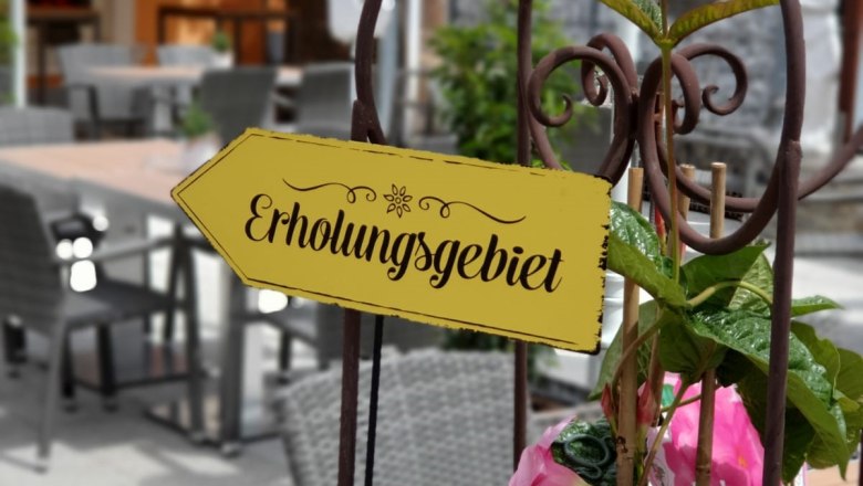 Ein Schild mit der Aufschrift 'Erholungsgebiet' in einem Café-Garten mit Tischen und Stühlen.