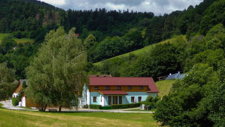 Ein Ferienhof mit roten Dächern in einer grünen, hügeligen Landschaft mit Bäumen und Wiesen.