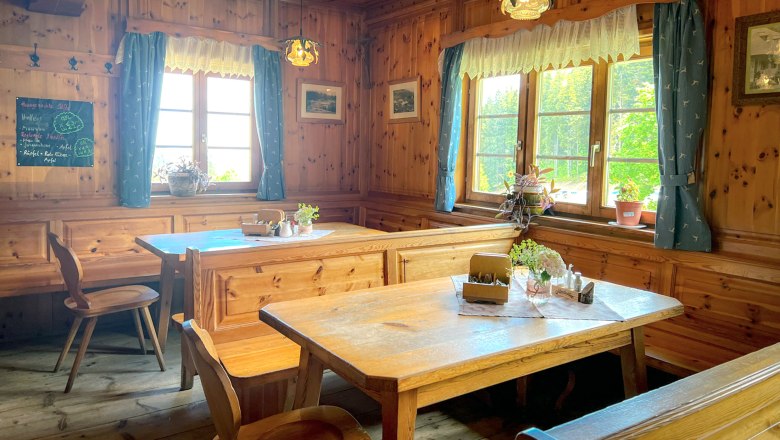 Gem&uuml;tliche Stube mit Holzm&ouml;beln, blauen Vorh&auml;ngen und Pflanzen auf den Tischen.