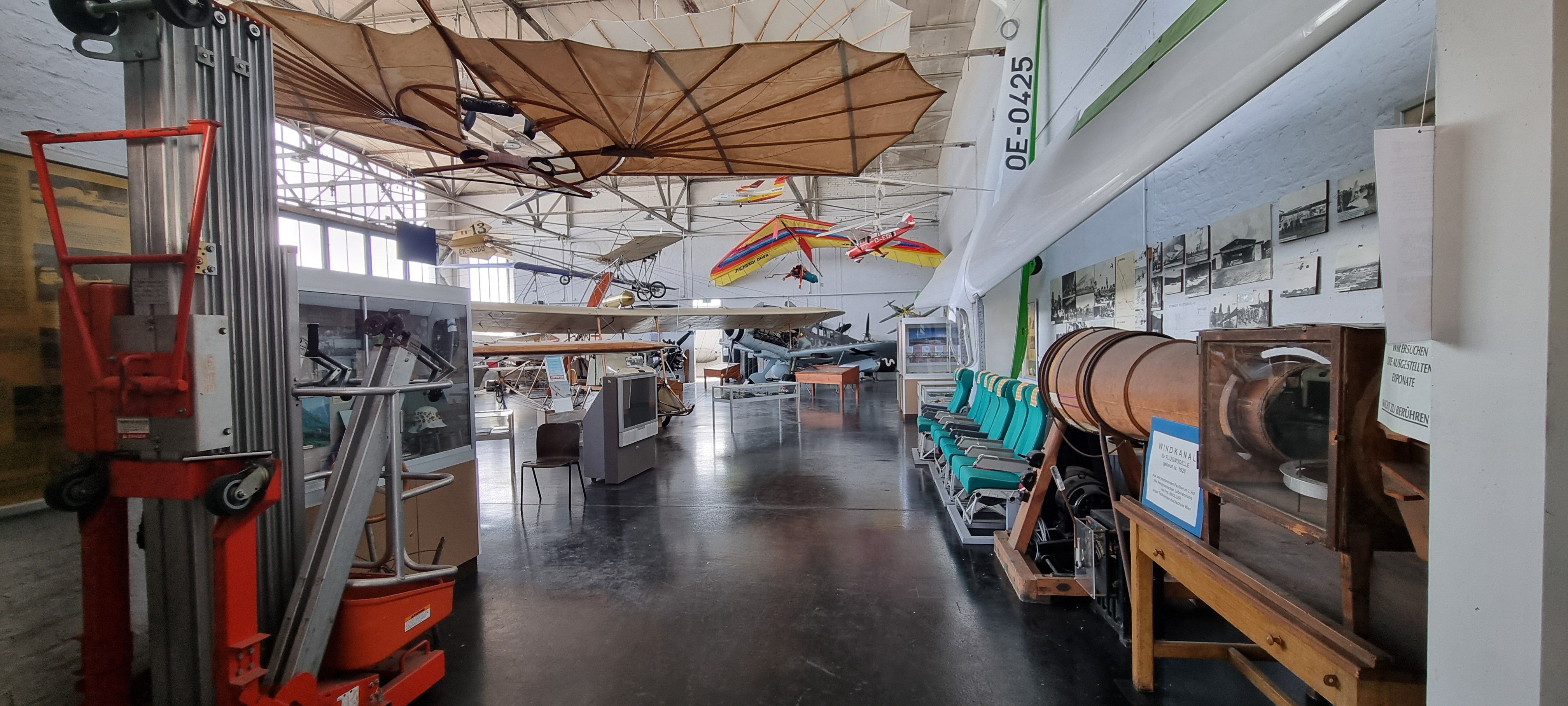Große Halle mit von der Decke hängenden Exponaten, Flugzeugsitzen, Informationsaufstellern und Fernsehern.