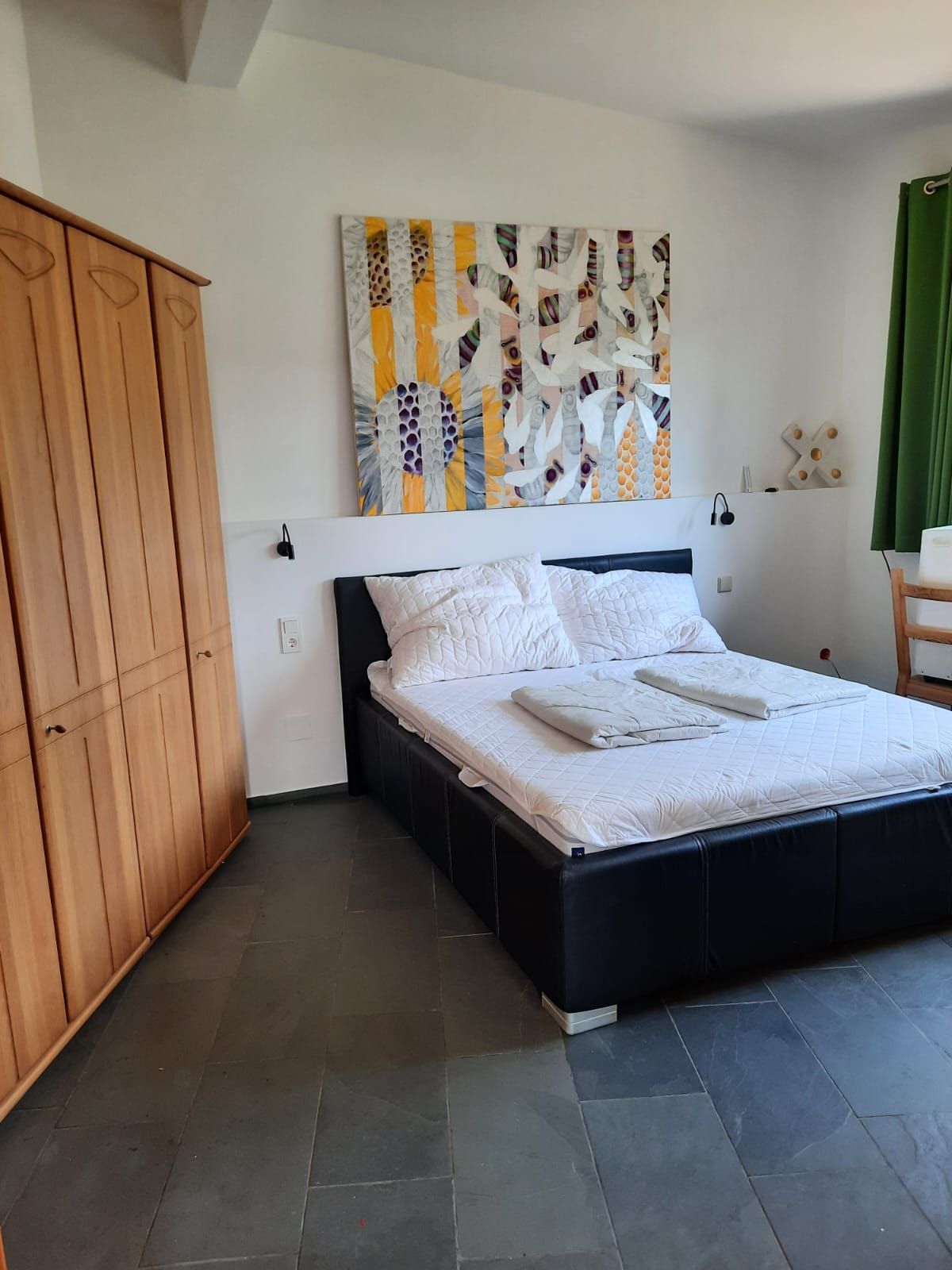 Schlafzimmer mit Doppelbett, Holzschrank und modernem Kunstwerk an der Wand.