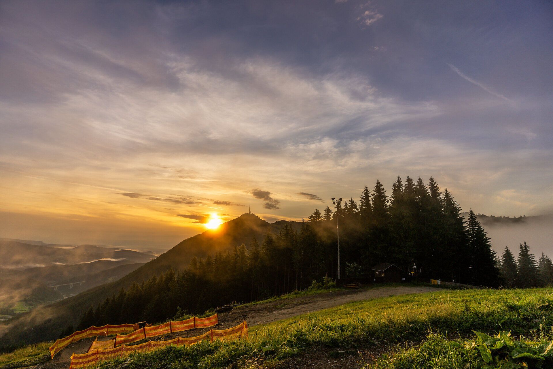 Ein atemberaubender Sonnenaufgang taucht die majestätischen Berge in goldenes Licht und lässt die umliegenden Wälder geheimnisvoll erstrahlen. Die frische Morgenluft und das sanfte Zwitschern der Vögel laden zu einer unvergesslichen Wanderung ein, während die Natur in voller Pracht erwacht.