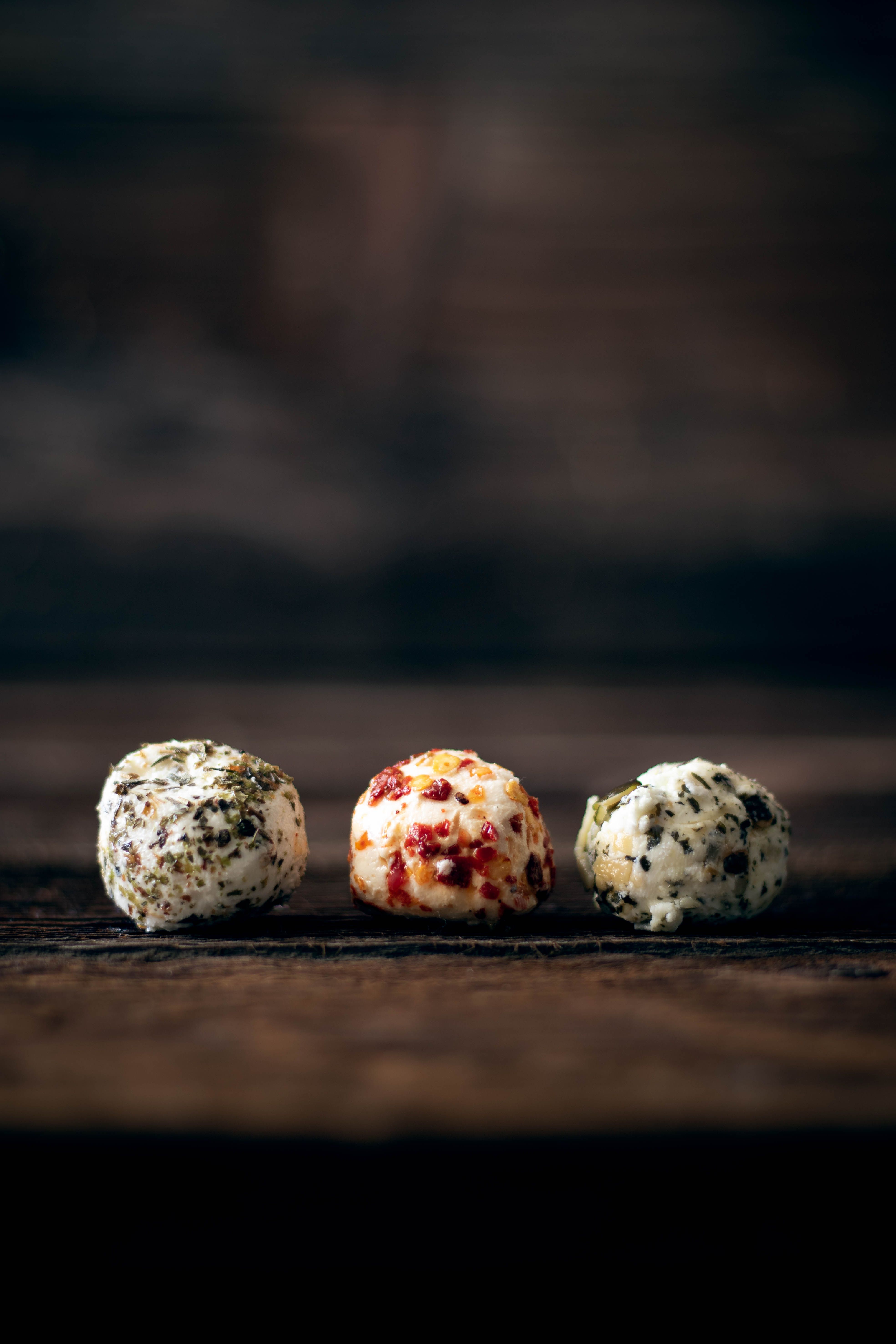 Drei Ziegenkäsebällchen mit Chilli, Kräutern und Kürbiskernen auf Holzuntergrund.