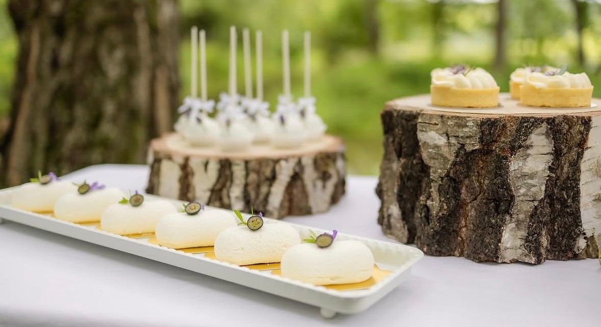 Desserts auf einer Tafel im Wald, serviert auf Baumstamm-Scheiben; im Vordergrund das kleine Süße auf einer weißen Platte.