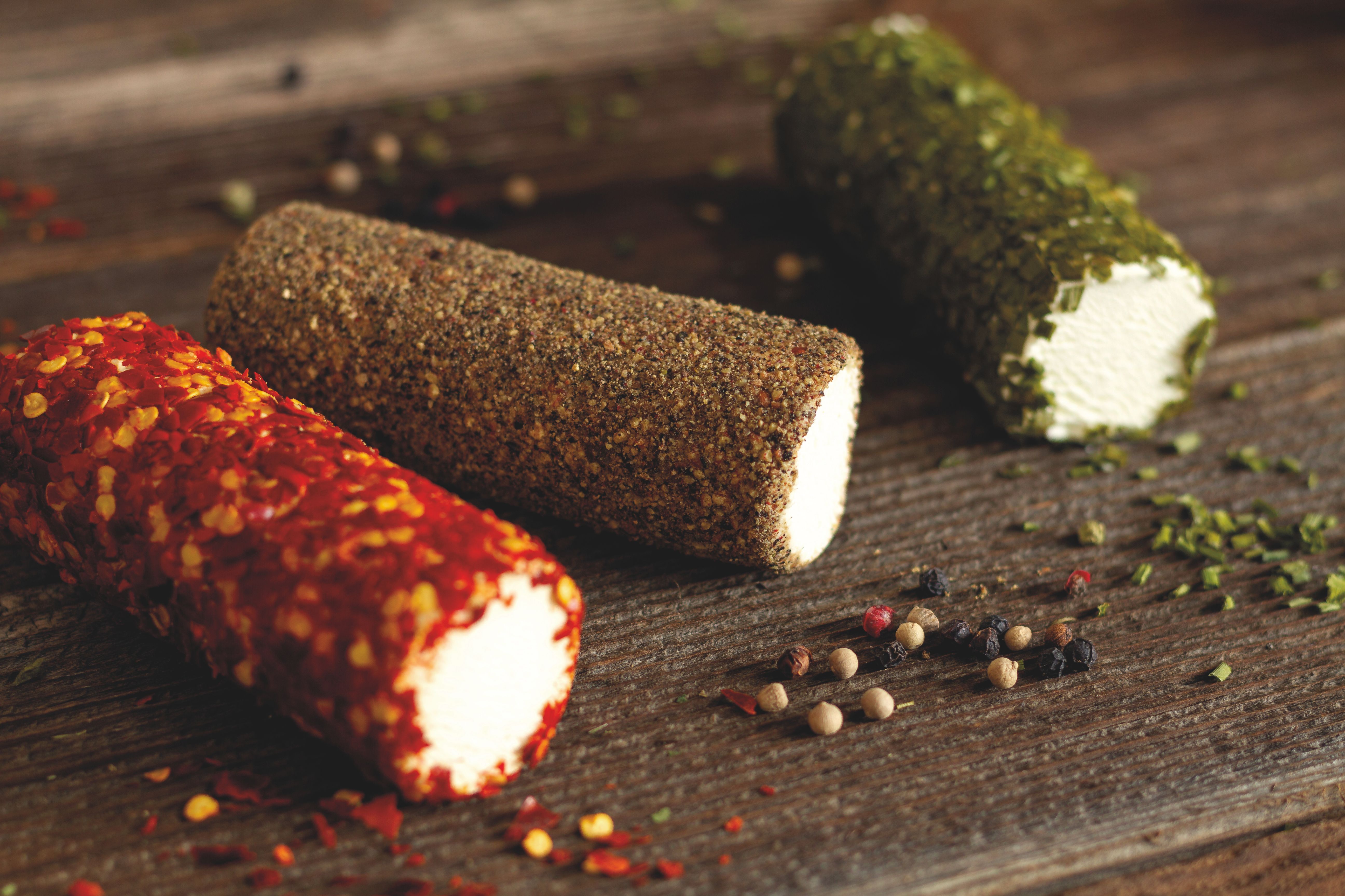 Drei Ziegenkäseröllchen mit Schnittlauch, Chilli und Pfeffer auf Holzuntergrund.