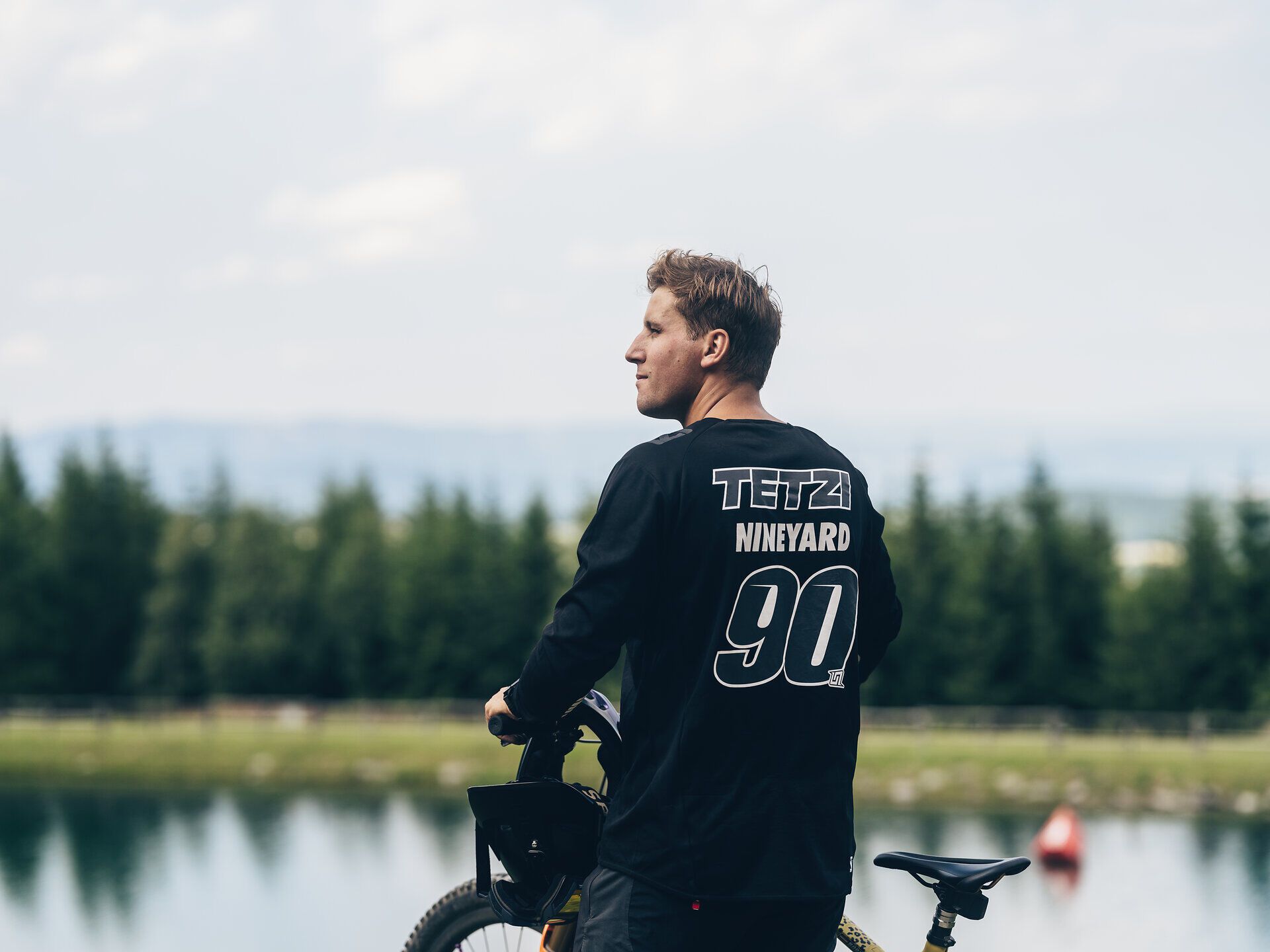 Ein Mountainbiker genießt die atemberaubende Aussicht auf die umliegenden Berge, während er sich auf den nächsten Trail vorbereitet. Die frische Bergluft und das sanfte Plätschern des Wassers im Hintergrund schaffen eine perfekte Kulisse für Abenteuer und Erholung in der Natur.
