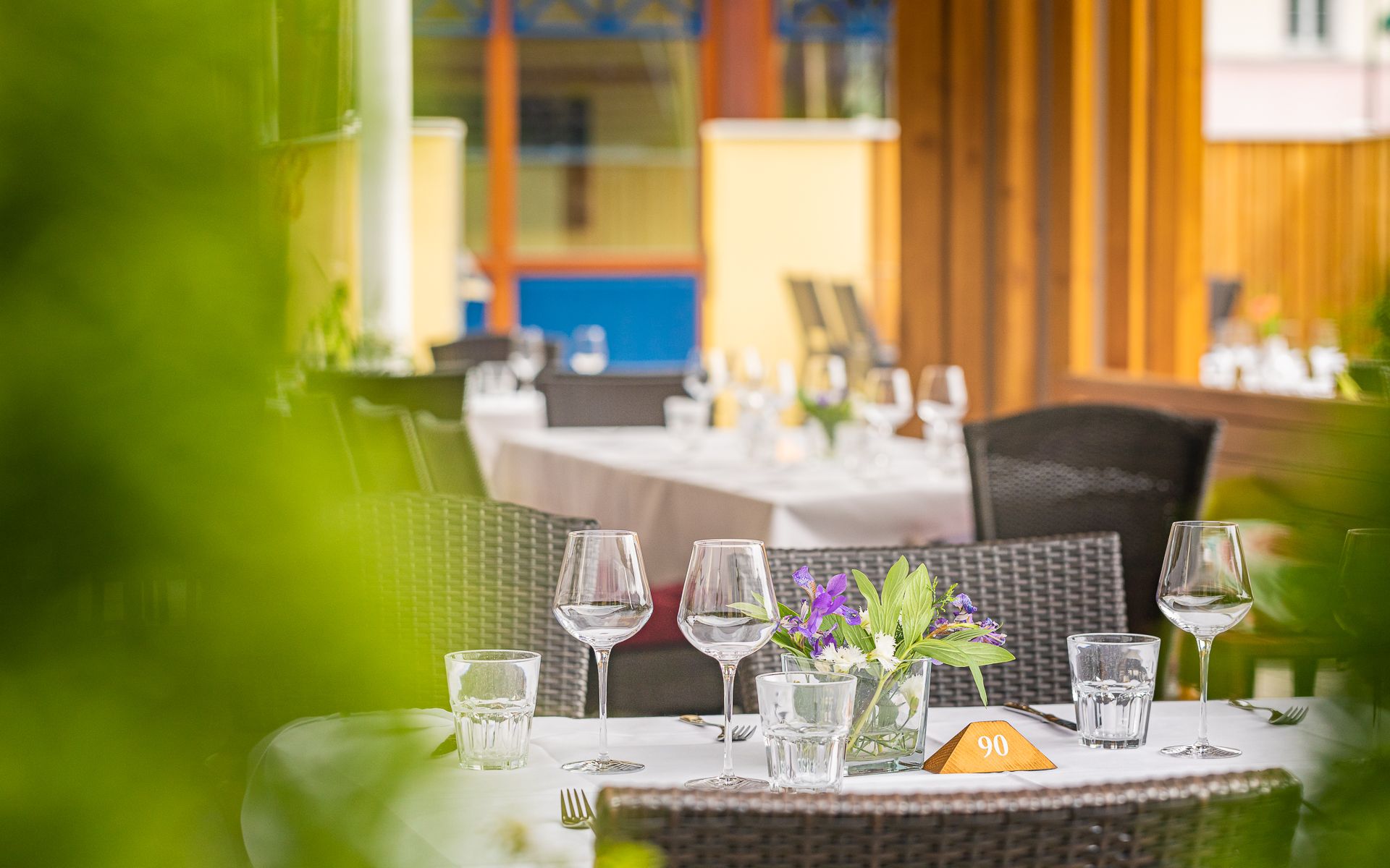 Gedeckter Tisch auf einer Restaurantterrasse mit Weingläsern und Blumendekoration.