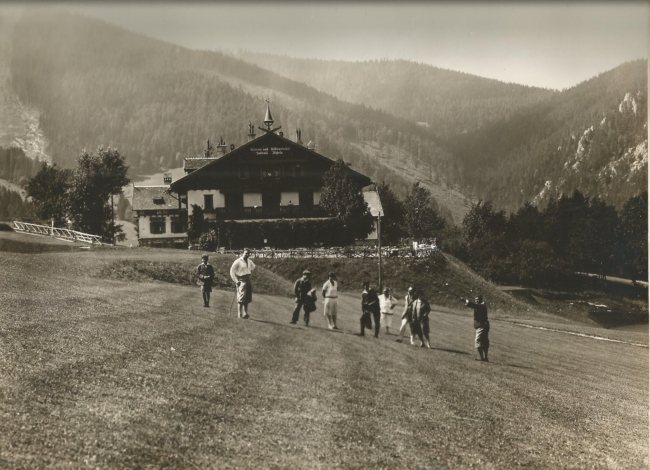 Golfspieler sind auf einem Golfplatz versammelt und ein Gebäude und Berge im Hintergrund
