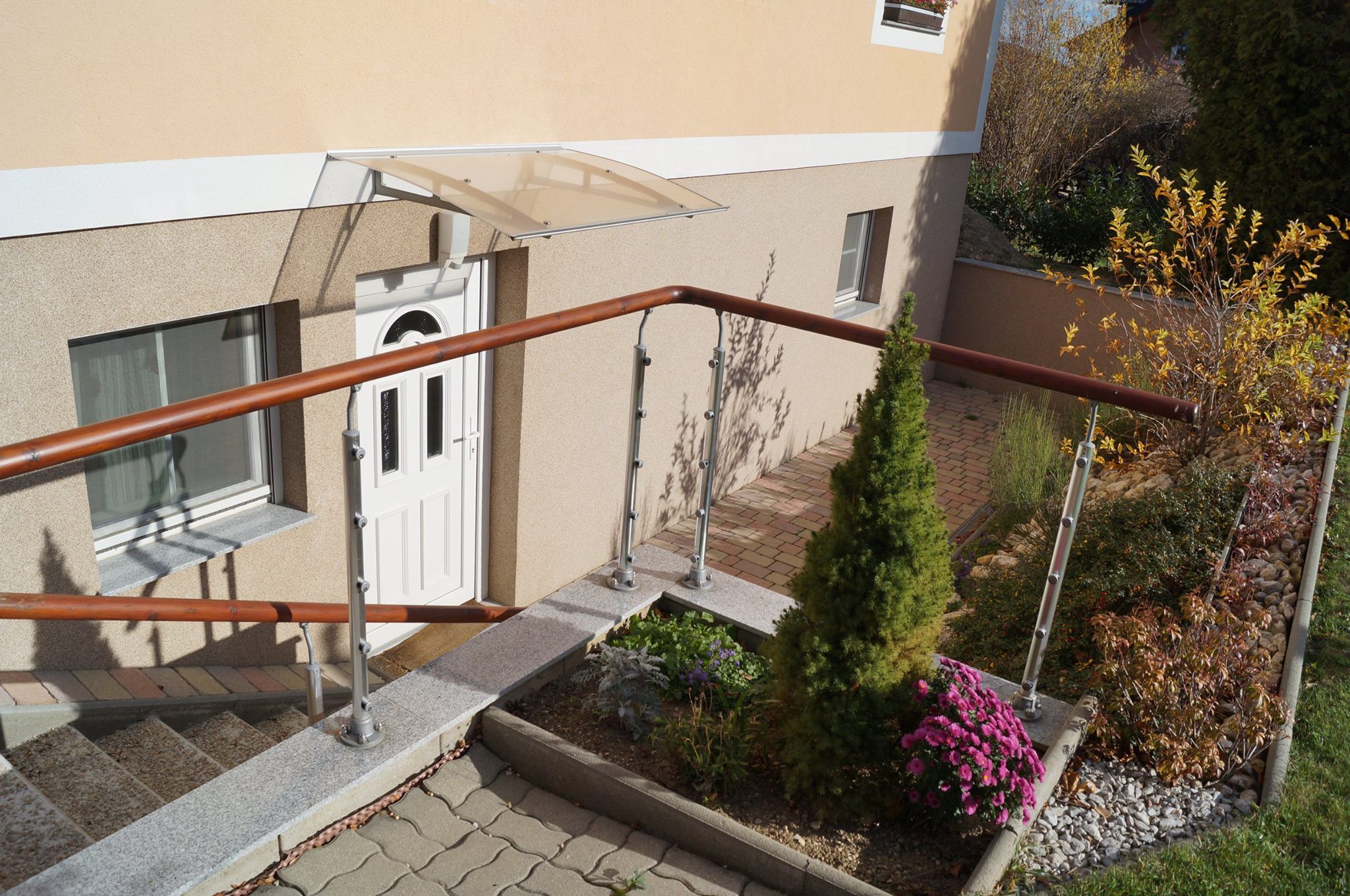 Eingangsbereich eines Hauses mit weißer Tür, Geländer und Garten.