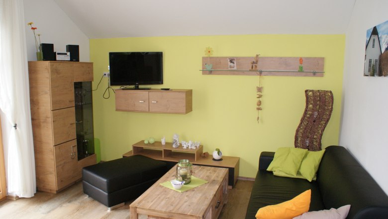 Modernes Wohnzimmer mit gelber Wand, schwarzem Sofa, Holzmöbeln und Dekorationen.