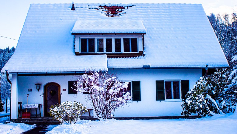 Ein verschneites Landhaus mit schneebedecktem Dach und Garten im Winter.