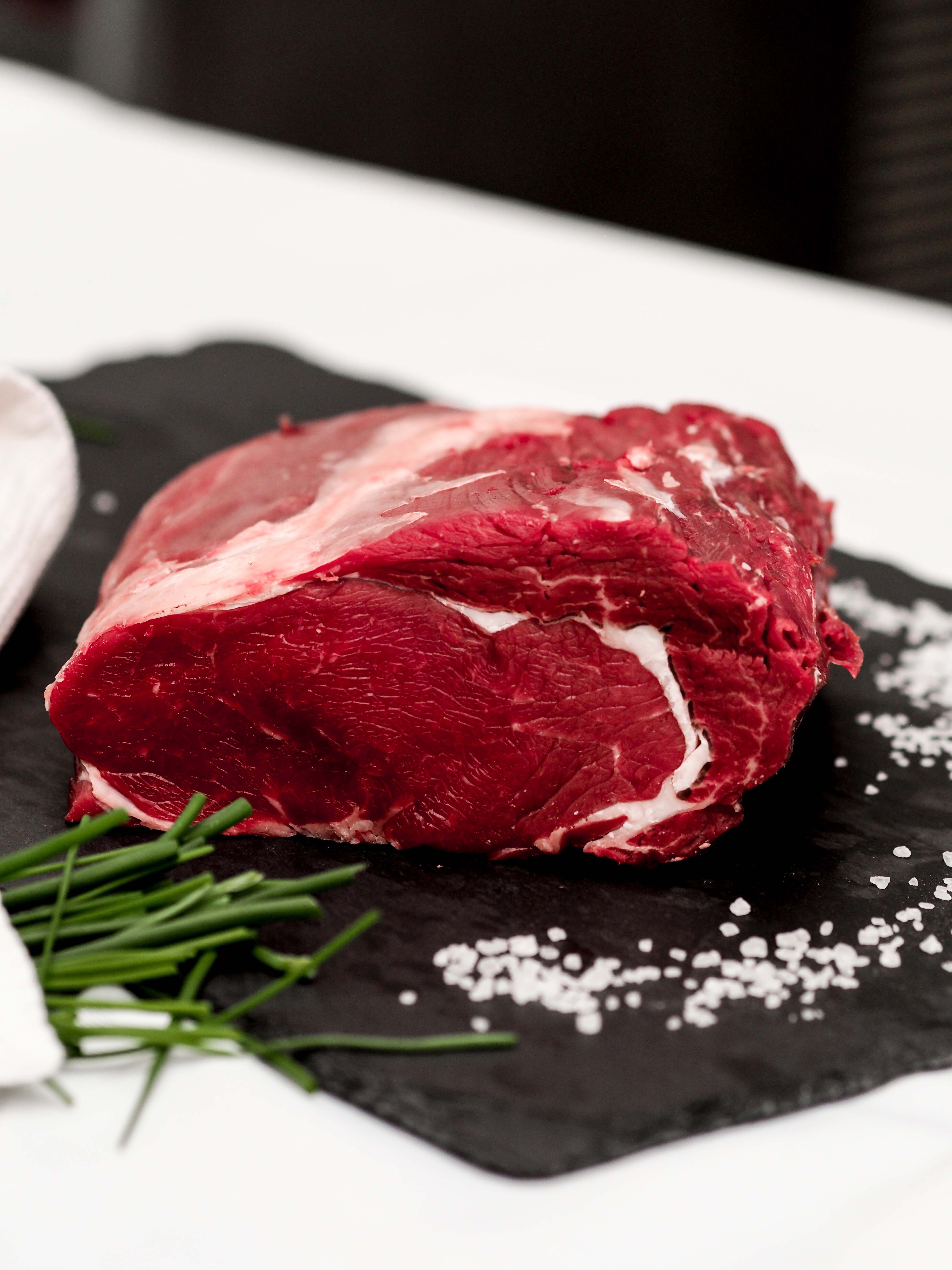 Ein rohes Stück Rindfleisch liegt auf einer dunklen Schieferplatte neben Salz und Schnittlauch.
