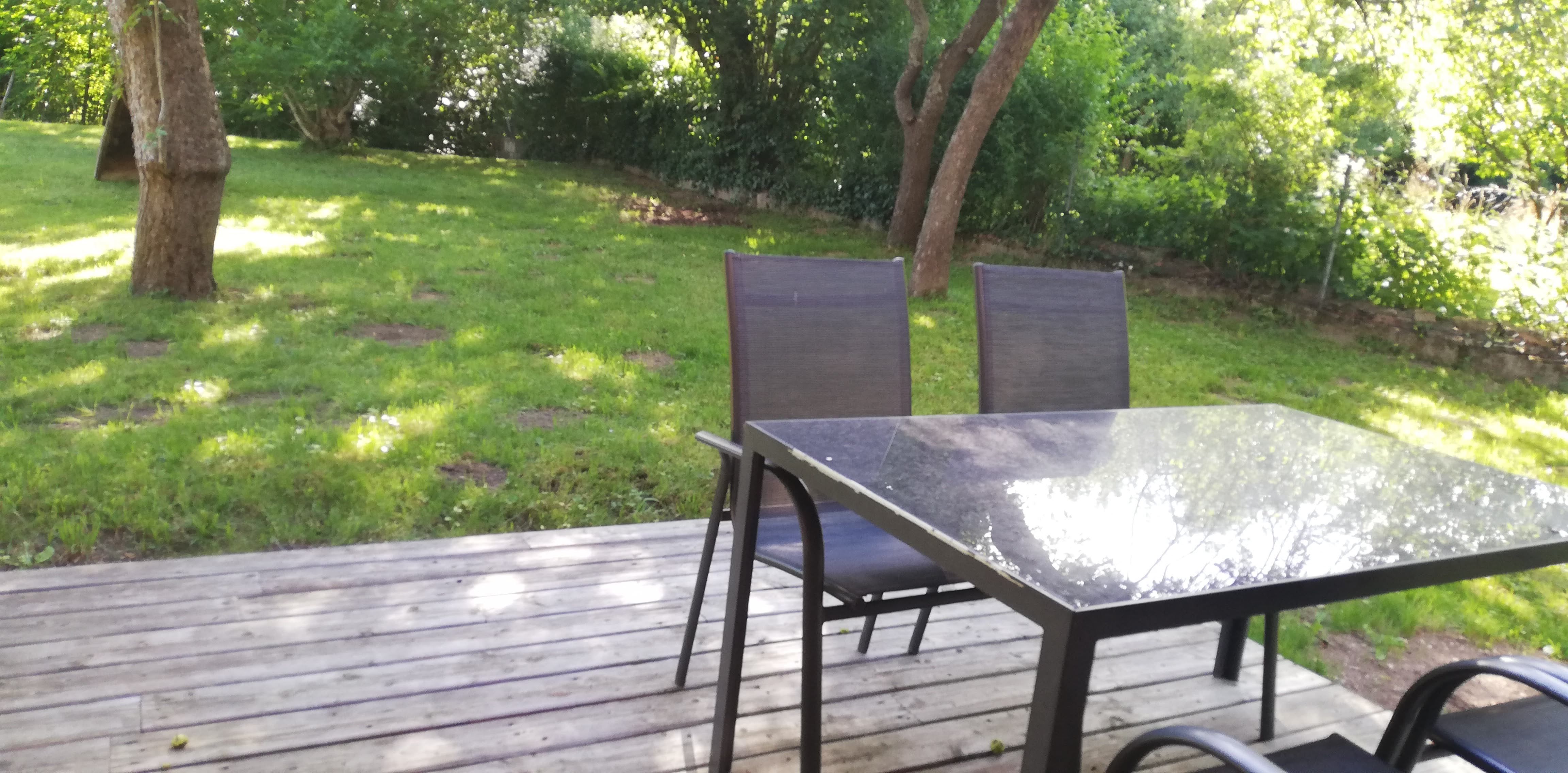 Terrasse mit Tisch und Stühlen, umgeben von grünem Garten.