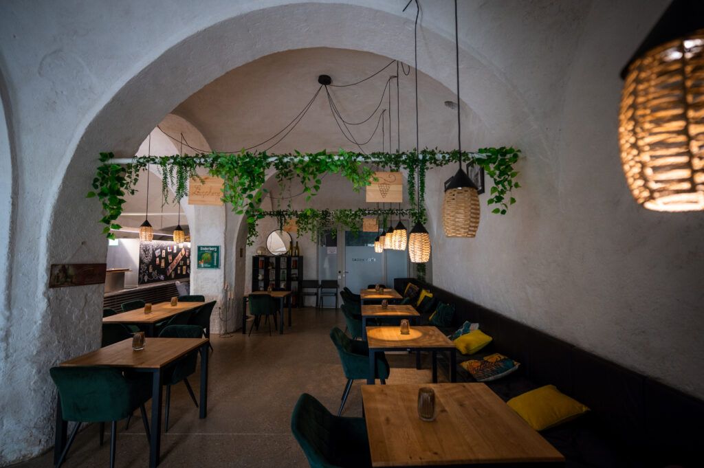 Innenansicht mit Tischen und Stühlen, sowie =Pflanzen, die von der Decke hängen