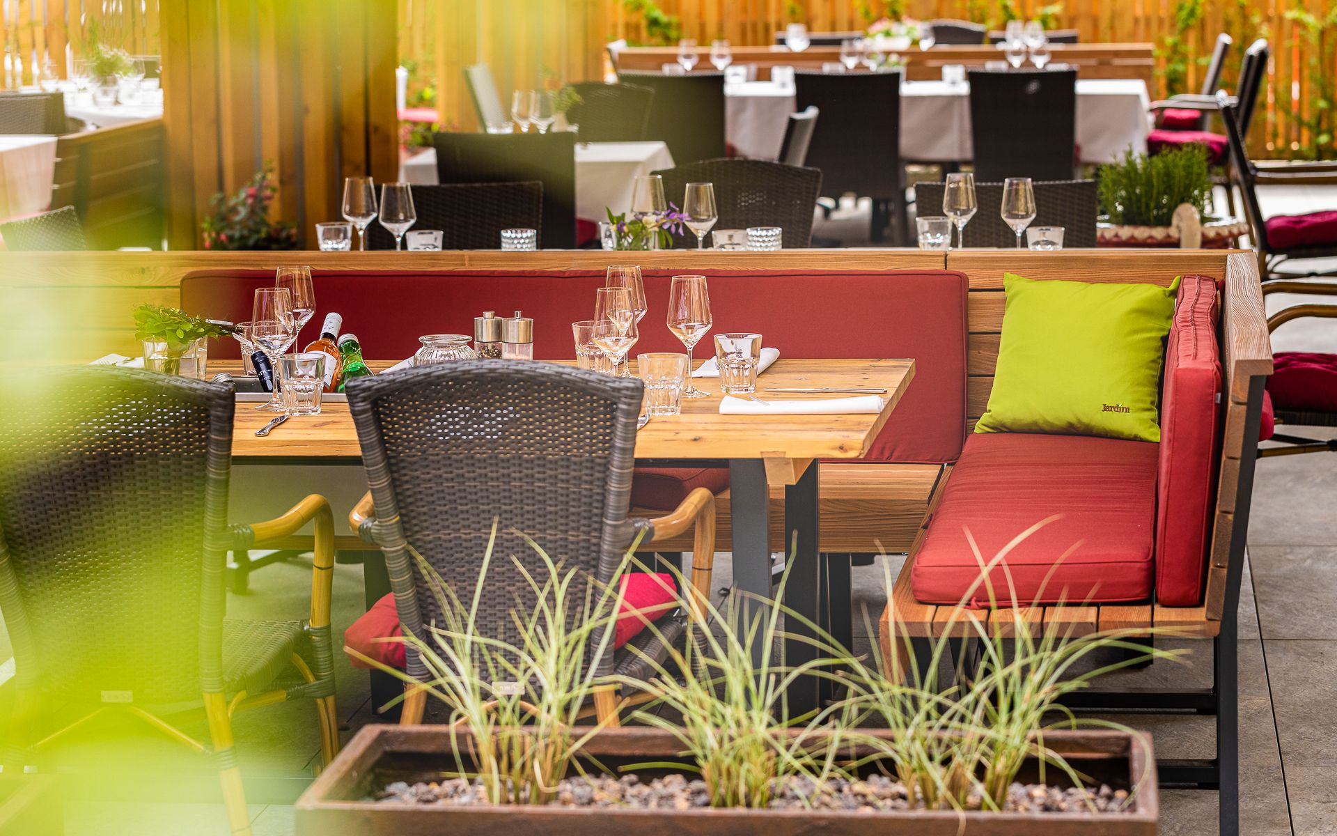 Gedeckter Tisch auf einer Terrasse mit roten Sitzpolstern und grünen Kissen.
