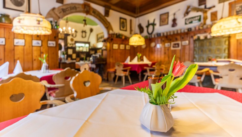 Gem&uuml;tliches Gastzimmer mit Holzm&ouml;beln, Tischdecken und Blumenvasen.