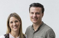 Ein Mann in Kochjacke und eine Frau im Dirndl vor einer weißen Wand. 