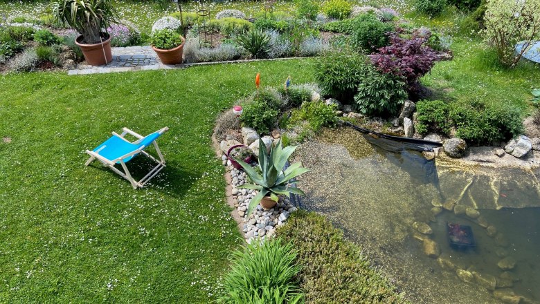 Garten mit Liegestuhl, Teich und Pflanzen.