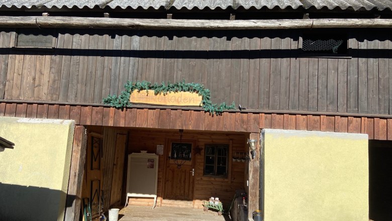 Entrance of a rustic farm store with wooden paneling and decoration made of fir branches.