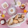 Breakfast table with bread rolls, cakes, cold cuts and drinks on a red and white checkered tablecloth.