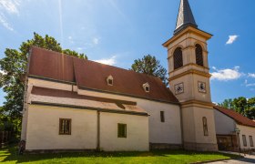 Kirche mit Turm und rotem Dach in Winzendorf bei Sonnenschein.