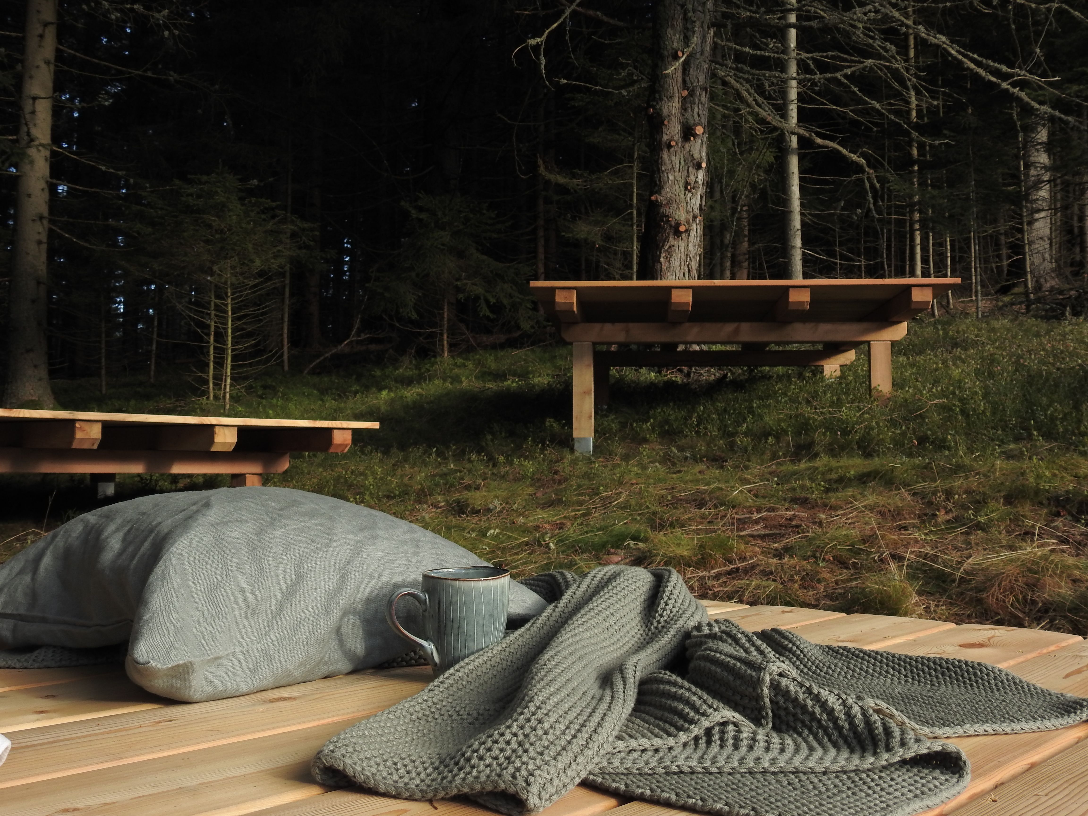 Holzplattform im Wald mit Kissen, Tasse und Decke.