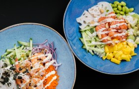 Zwei blaue Schalen mit hawaiianischen Bowls, gefüllt mit Lachs, Garnelen, Mango, Gurken, Edamame und Soßen.