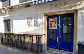 Eingang zur Bar GMBH mit blauer Tür und Werbeplakat.