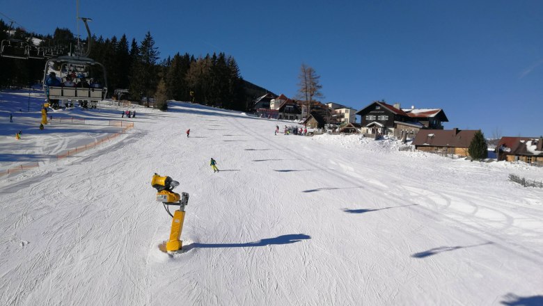 Skifahrer auf einer sonnigen Piste in Mönichkirchen mit Sessellift und Schneekanonen.