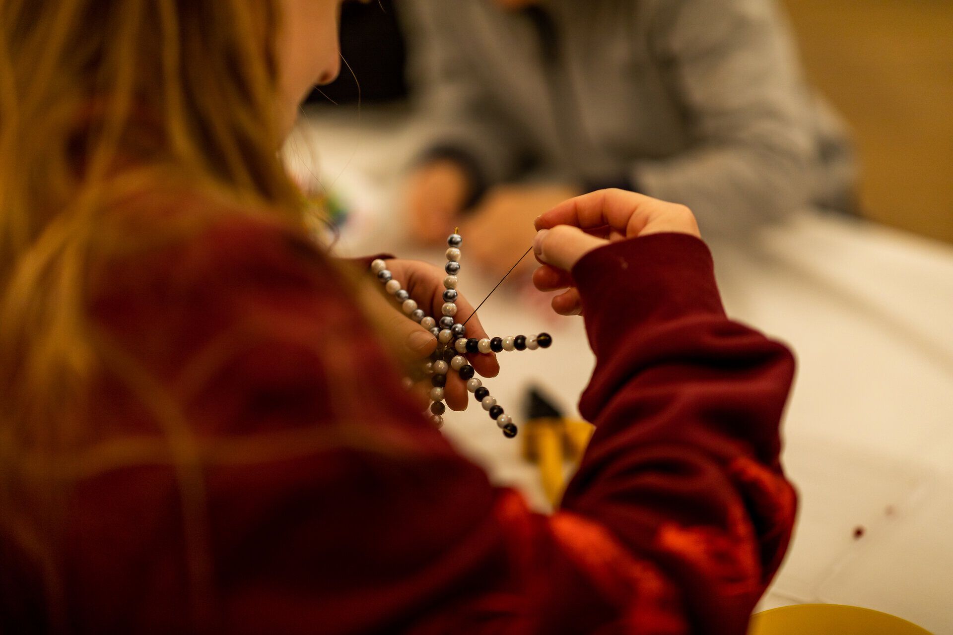 Person fädelt Perlen bei einer Bastelaktion in gemütlicher Atmosphäre.