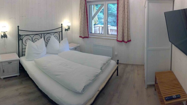 Schlafzimmer in einem Ferienhaus mit Doppelbett, TV und Fenster mit Vorhängen.