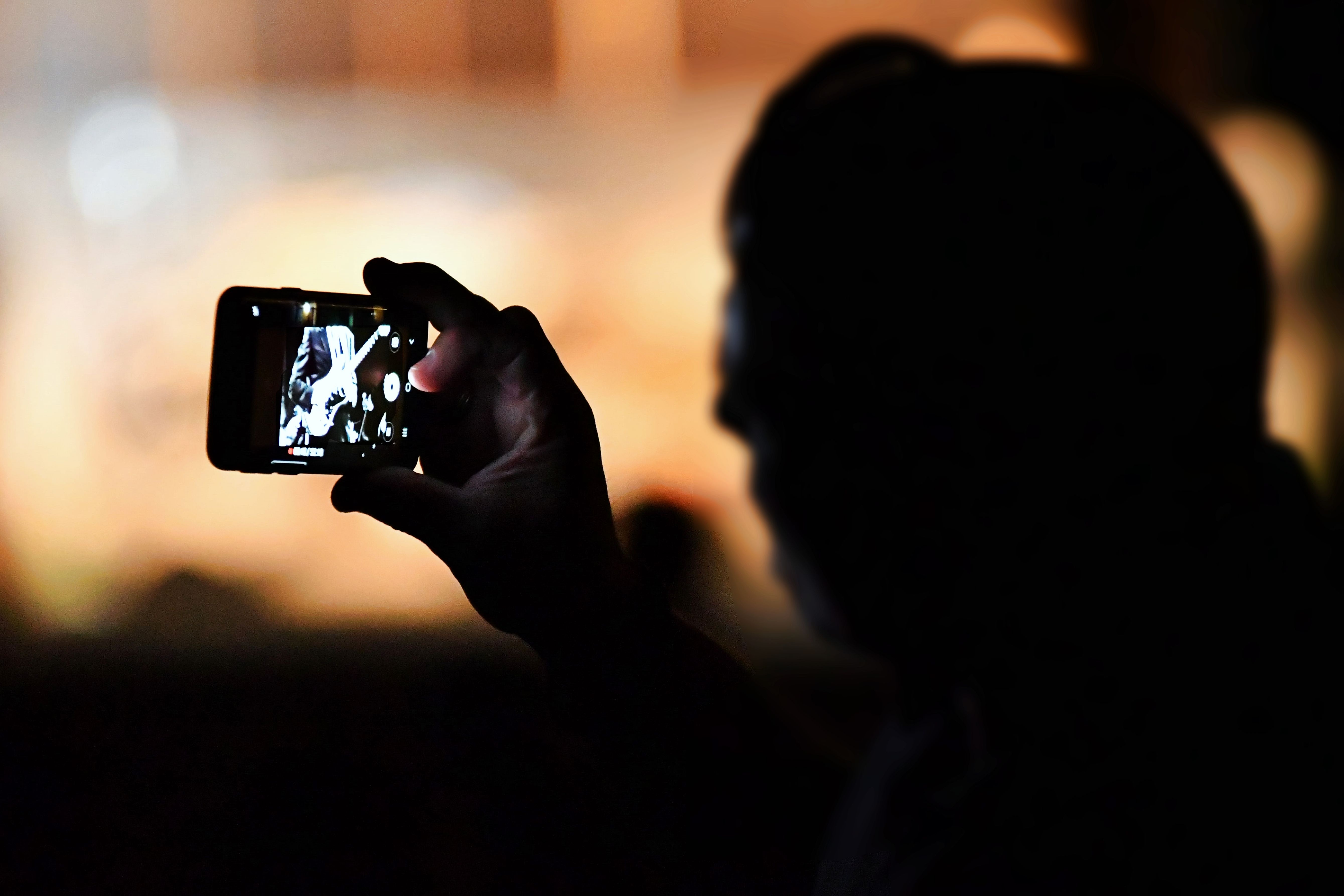 Silhouette einer Person, die in einer Menschenmenge ein beleuchtetes Ereignis mit dem Smartphone filmt oder fotografiert.