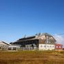 Panoramic view of a mountain hut with surrounding peaks under a blue sky.