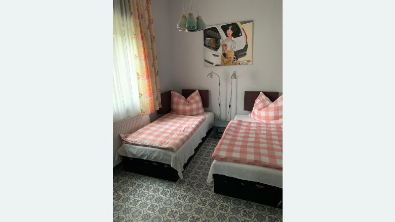 Zwei Einzelbetten mit rosa-weiß karierten Bettdecken in einem Schlafzimmer mit gemustertem Boden und einem Bild an der Wand.