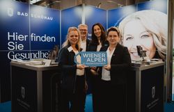 Drei Damen und ein Herr mit dem Schild Wiener Alpen in Niederösterreich vor dem Messestand Bad Schönau 