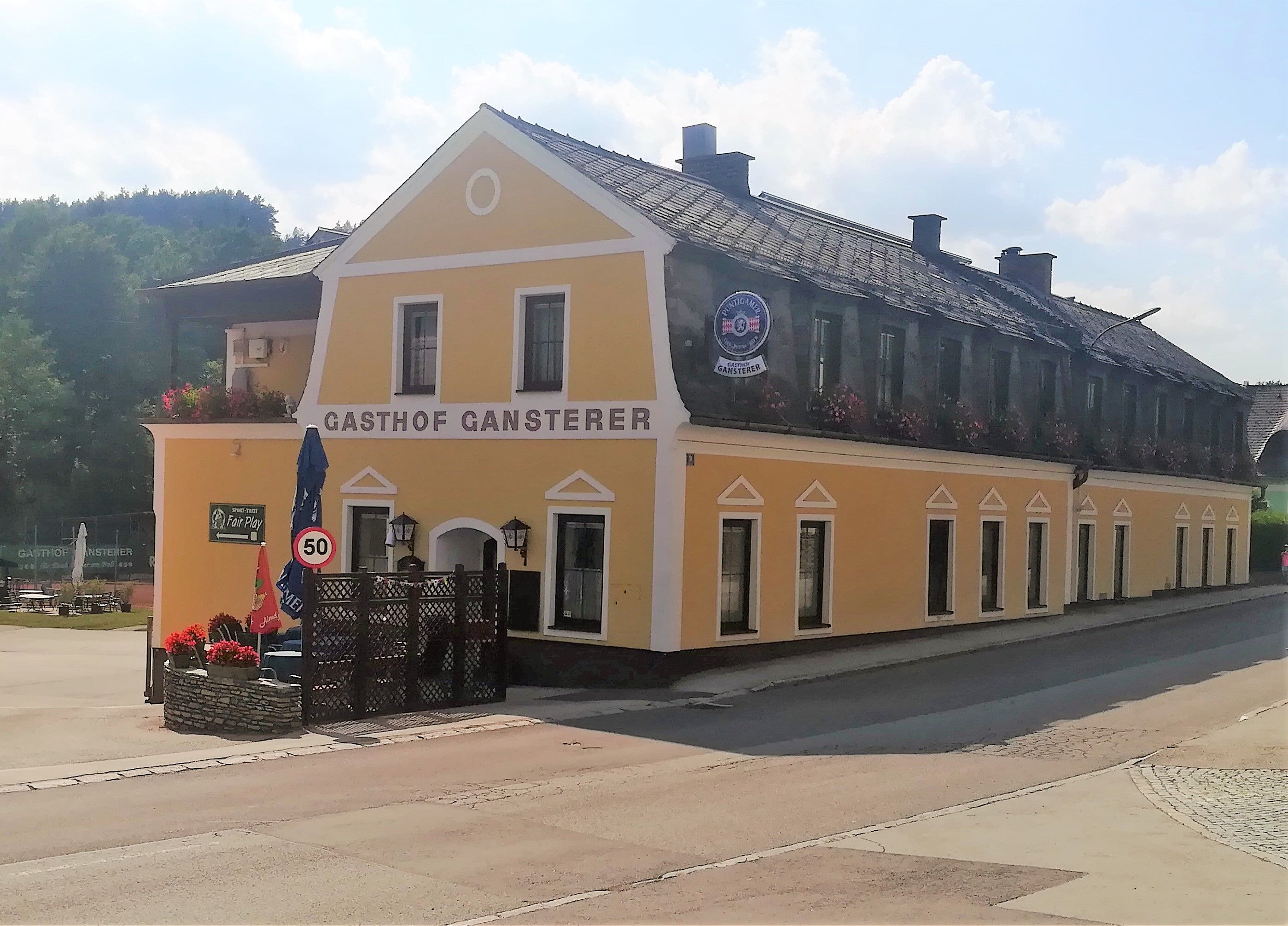 Gelbes Gebäude des Gasthofs Gansterer in Zöbern mit Blumenkästen und Verkehrsschild.