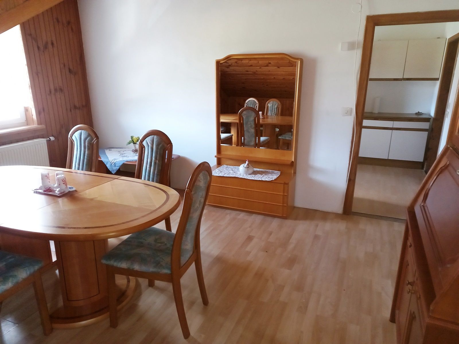 Esszimmer mit Holztisch, Stühlen und Spiegel, Blick in die Küche.