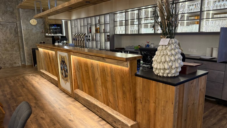 Holztheke in einem Restaurant mit dekorativer Vase und Gläserregal im Hintergrund.