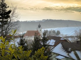 Winterliche Landschaft in Hollenthon mit schneebedeckten D&auml;chern und einer Kirche im Hintergrund.