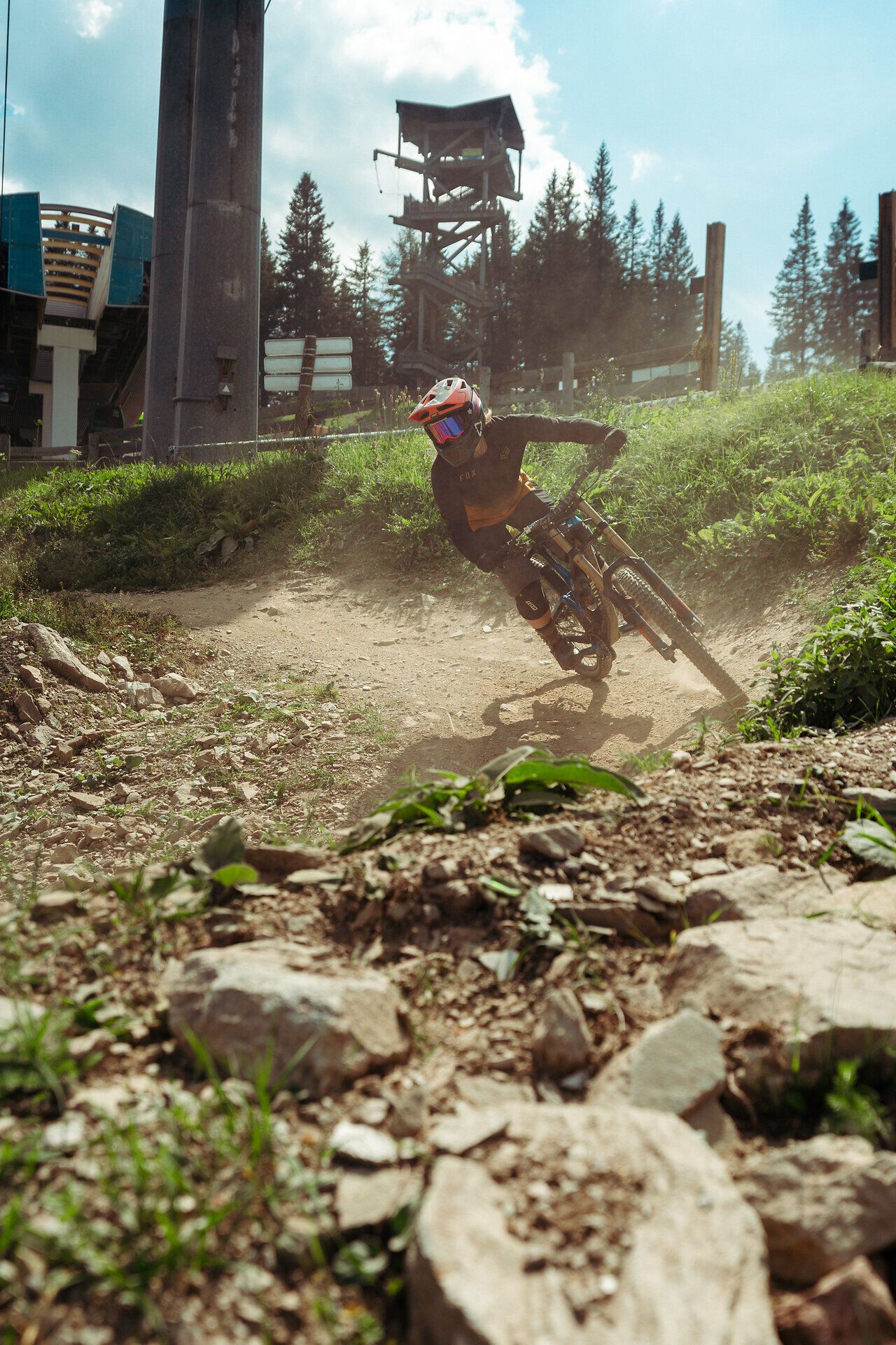 Mountainbiker fährt mit hoher Geschwindigkeit über einen steinigen Trail nahe einer Bergstation und wirbelt Staub auf.